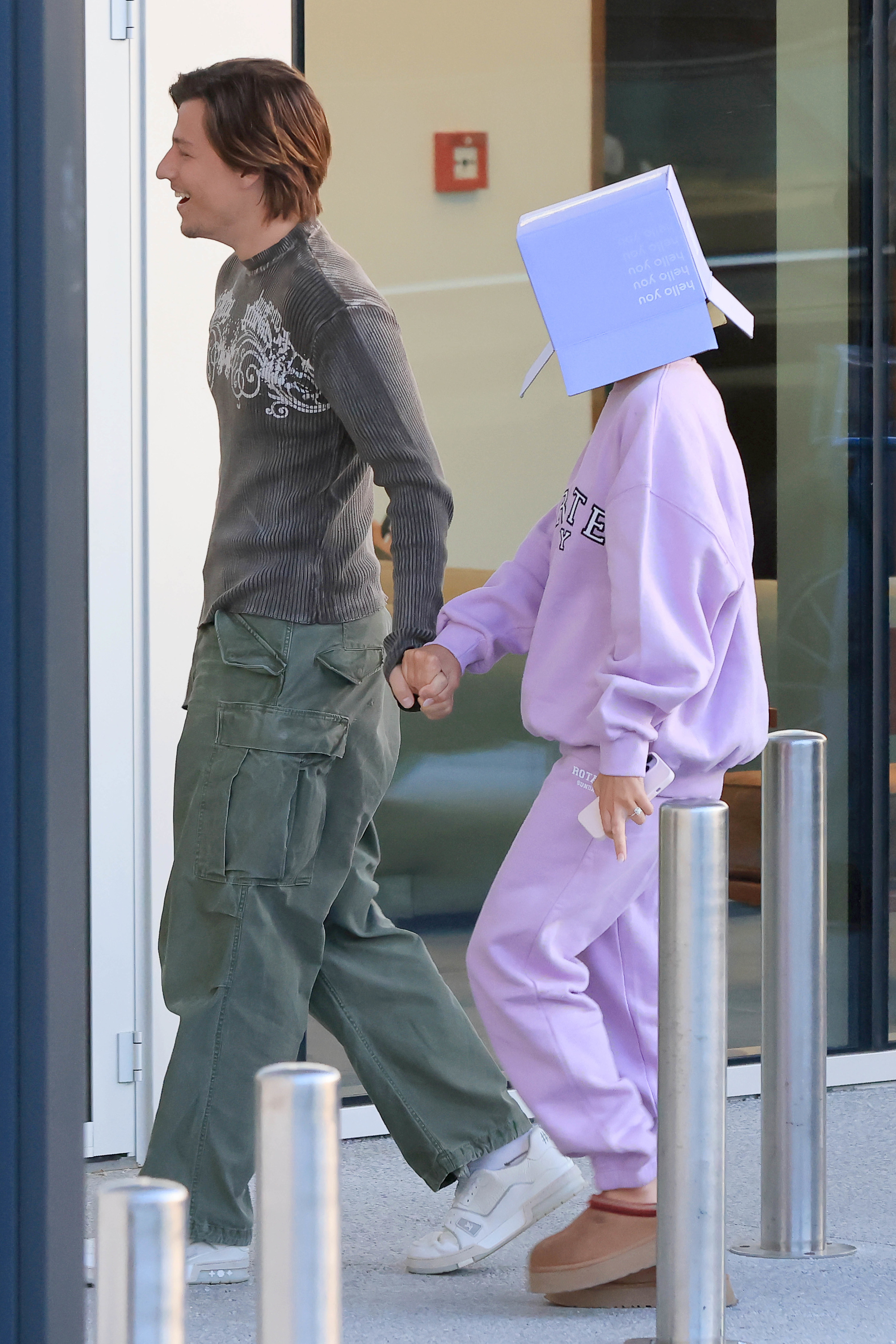 Jake Bongiovi and Millie Bobby Brown walking down the street, a box covering her head