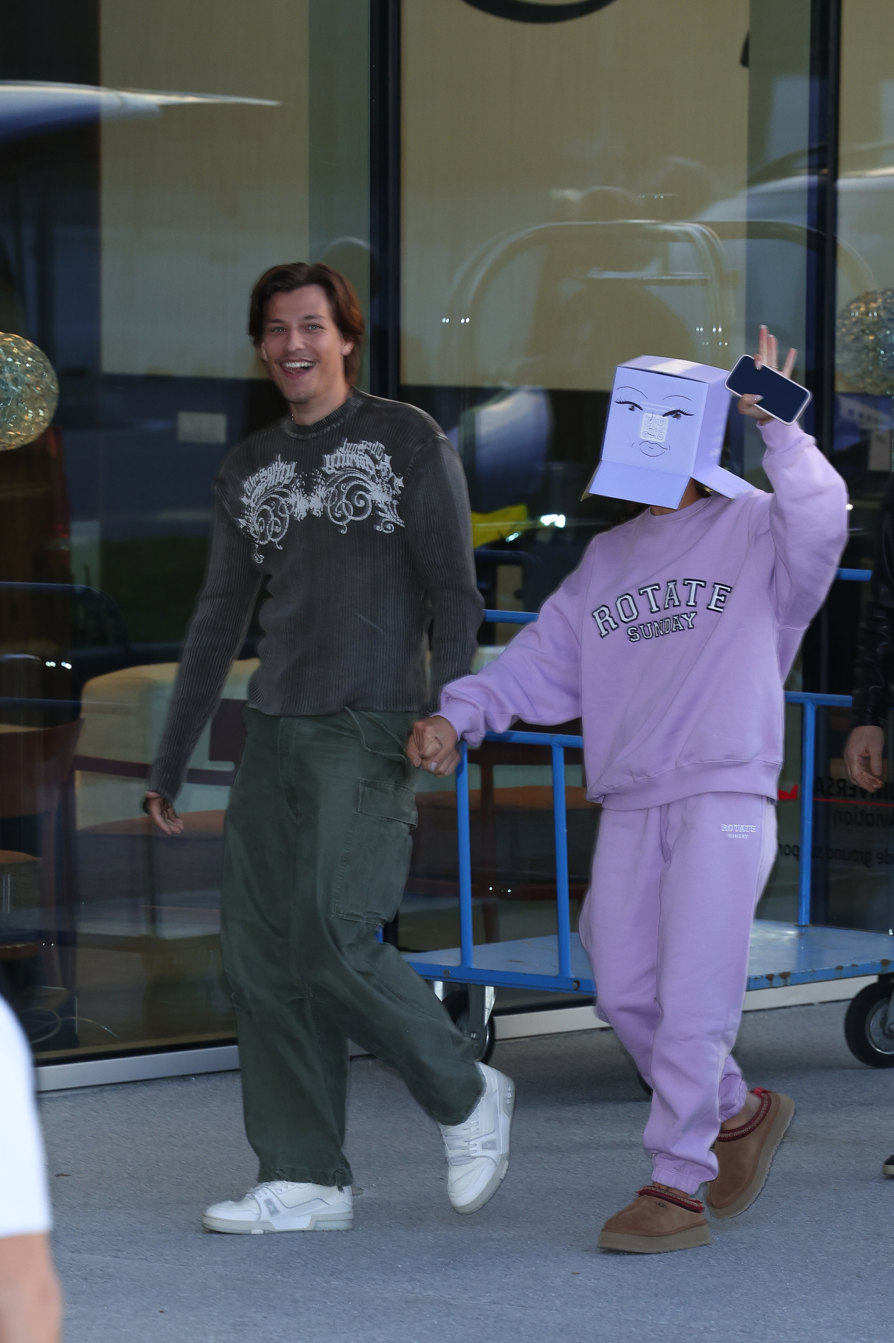 Jake Bongiovi and Millie Bobby Brown walking down the street, a box covering her head