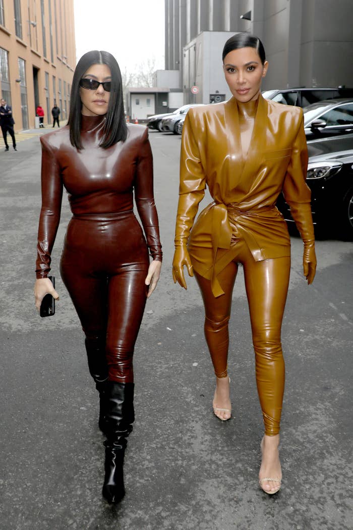 Kourtney and Kim Kardashian walking down the street. They&#x27;re both wearing leather jumpsuits