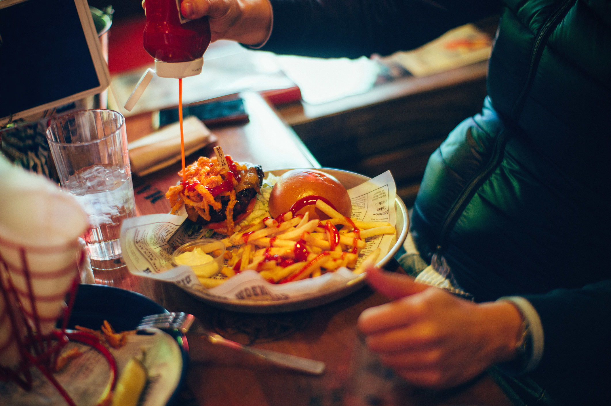A person squeezing ketchup onto a burger