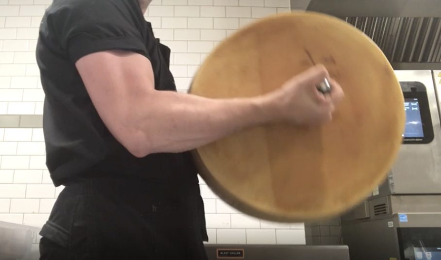 A person with large biceps lifting a Parmesan wheel