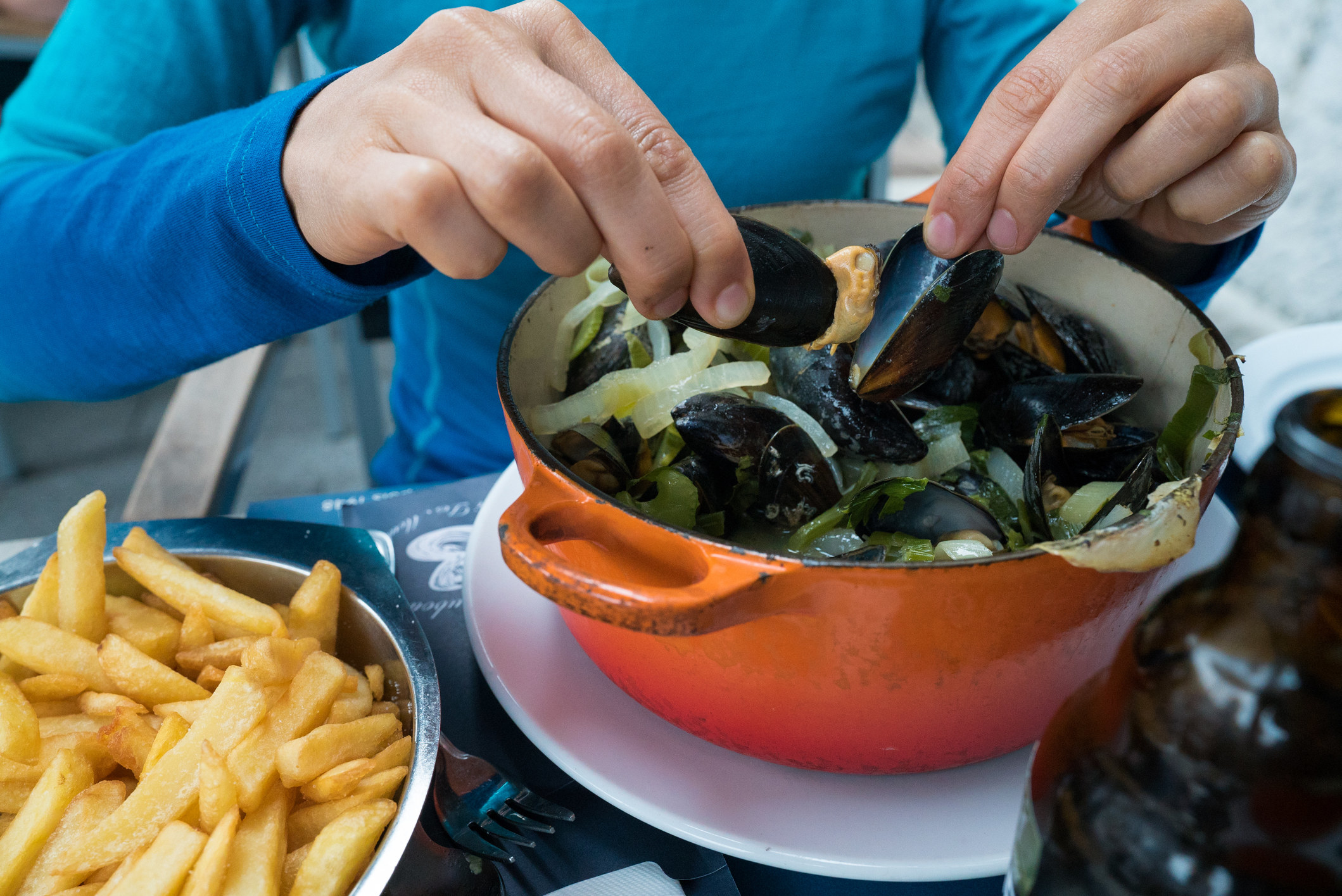 Hands of a woman eating traditional dish of mussels and french fries
