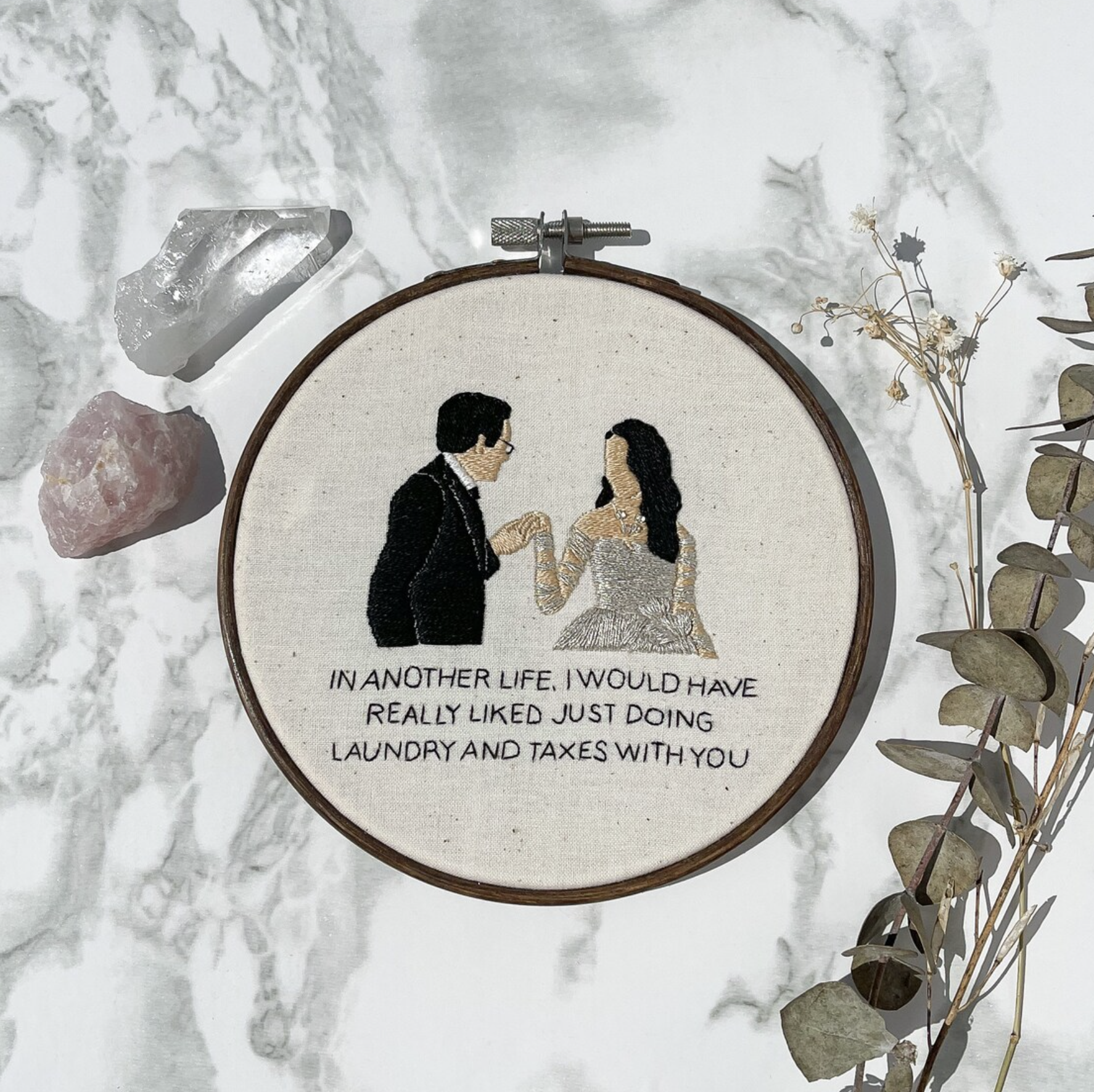 Embroidery hoop featuring Evelyn and Waymond Wang with "Laundry and Taxes" quote