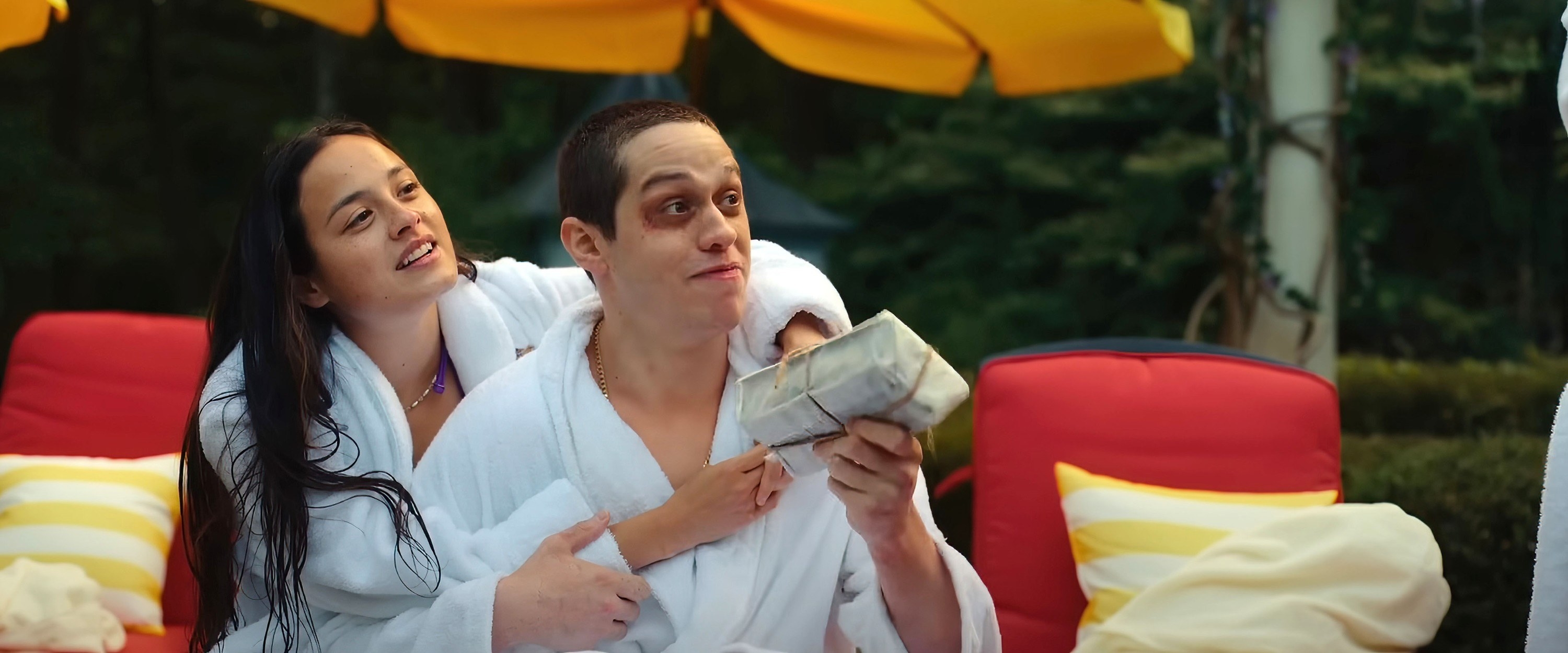 Chase holds Pete from behind as they lounge by the pool in bathrobes in a scene from Bodies
