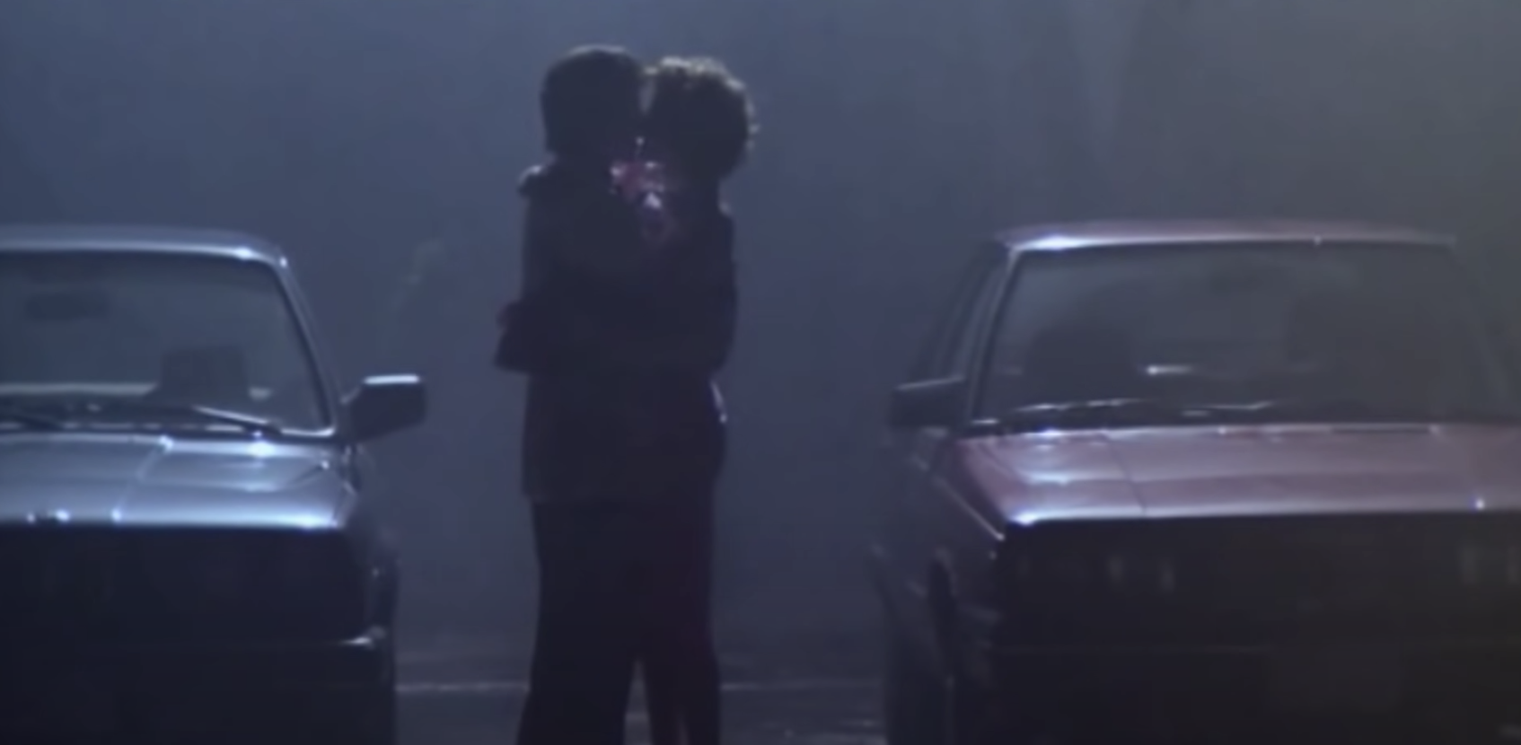 A man and woman embrace in a parking lot