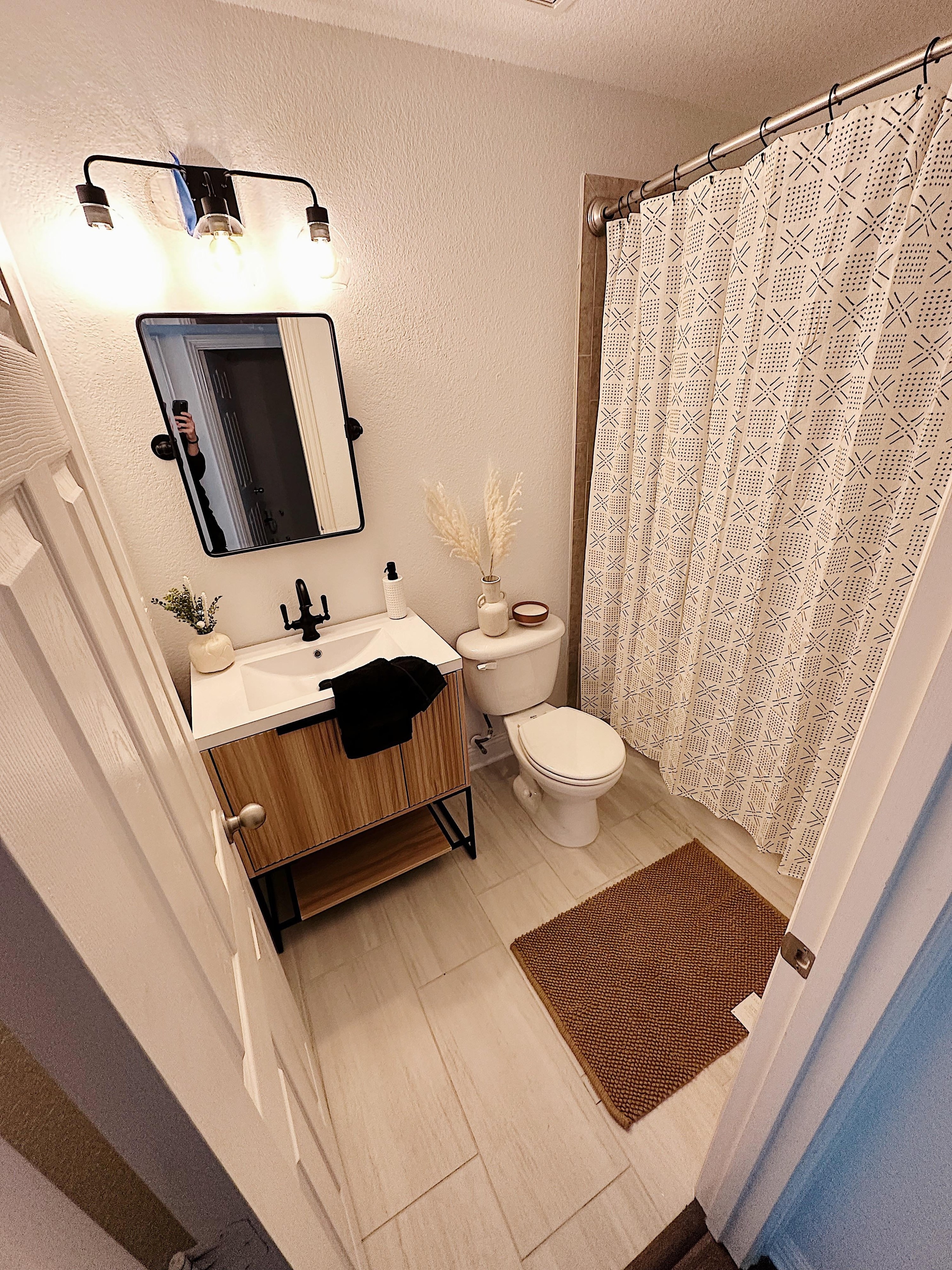 new renovated bathroom with laminate tile, matte black vanity mirror, and new vanity cabinet