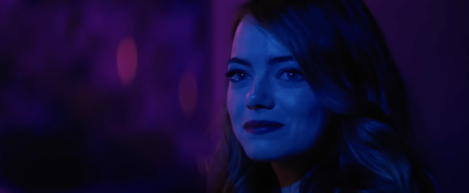 A woman in blue lighting smiles at someone off screen