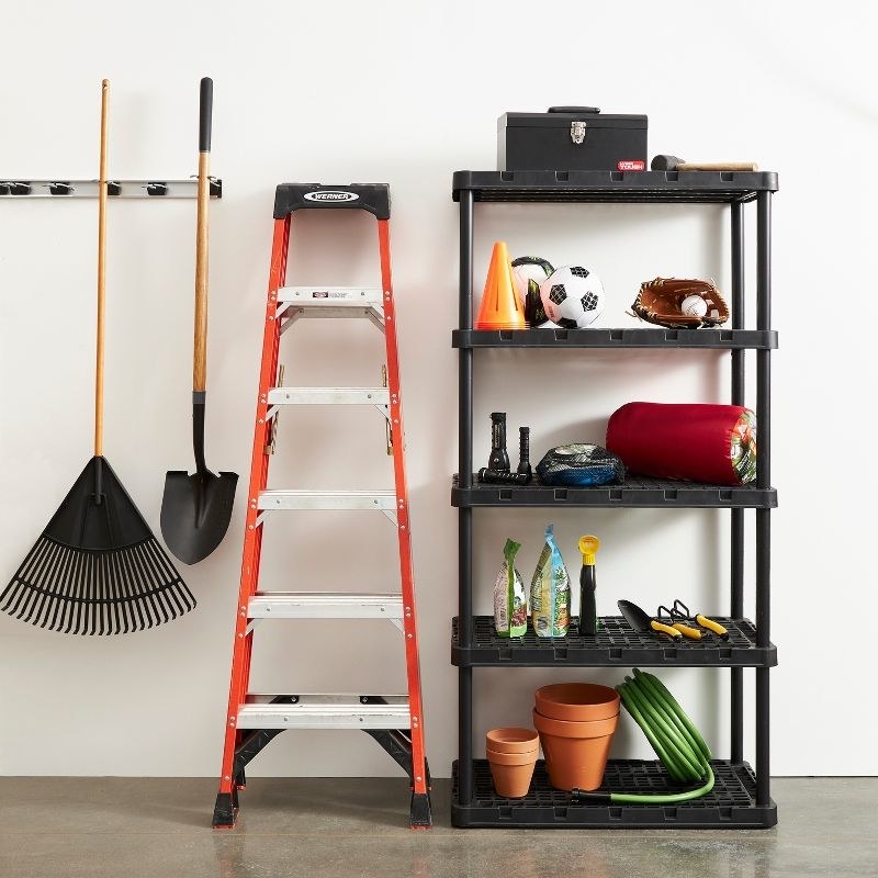 a five-tier black storage shelf in a garage holding up pots, sports equipment, and gardening tools