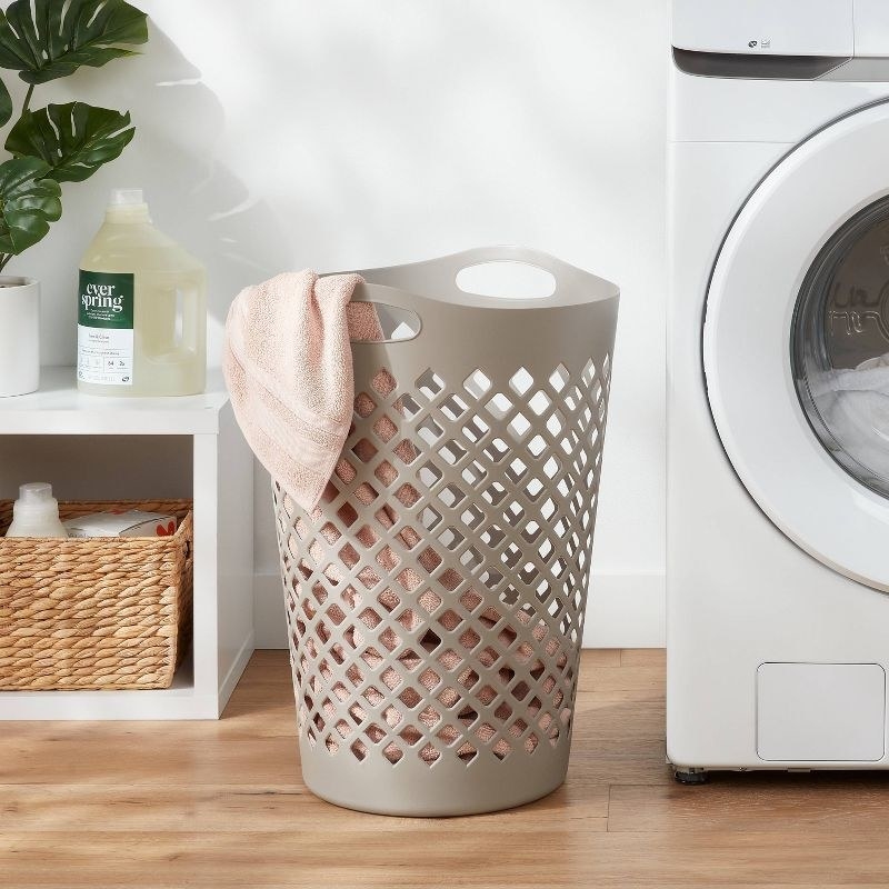 a tan-colored laundry hamper on a hardwood floor next to a white dryer