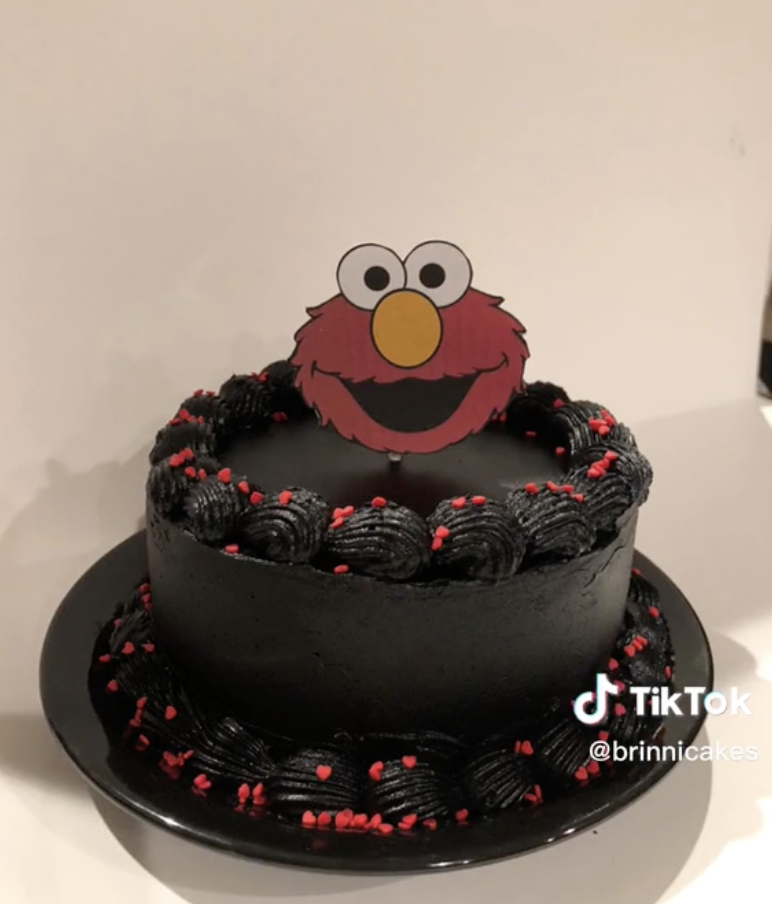 A completely black cake with red heart sprinkles and an Elmo topper