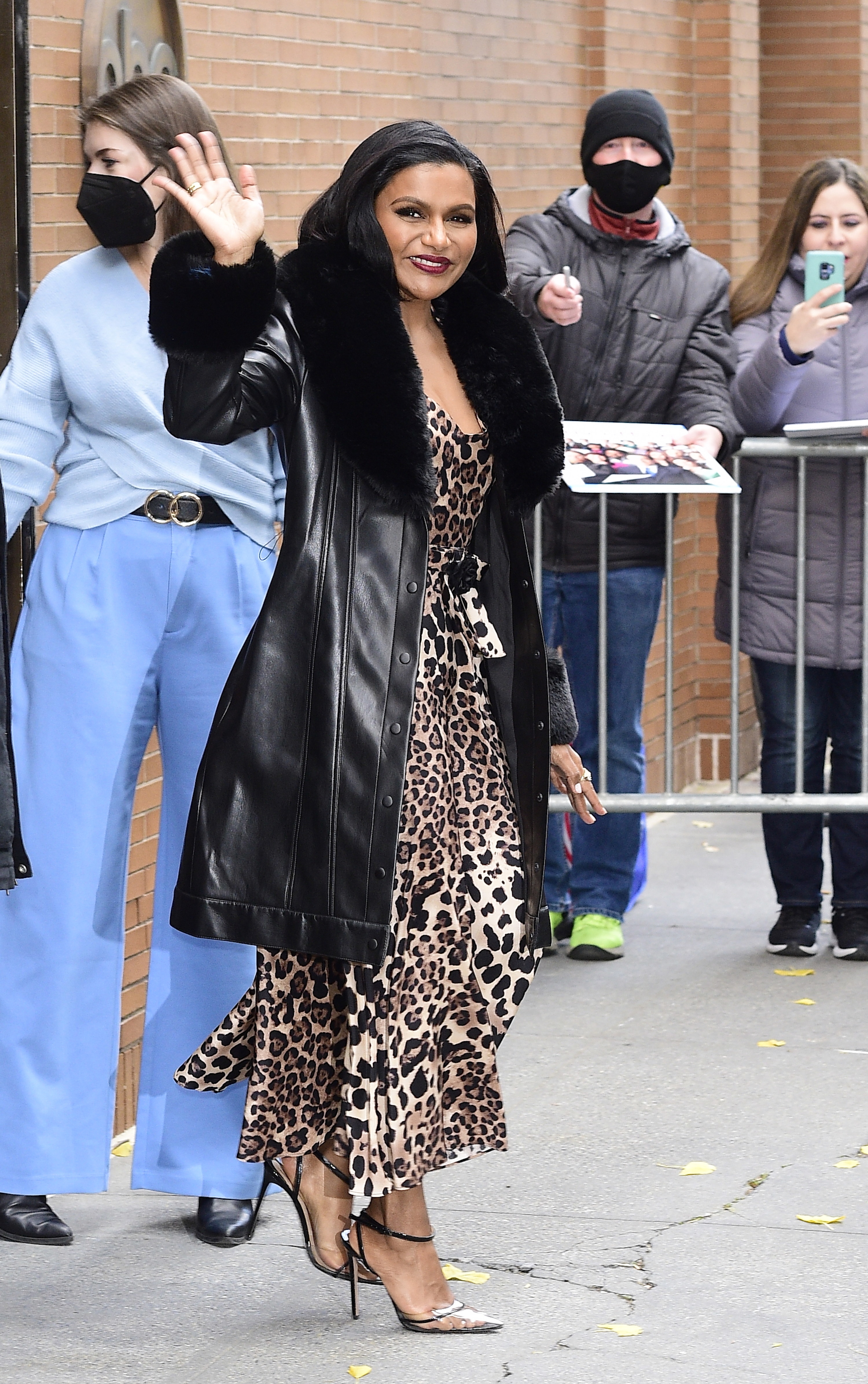 Mindy waves to a crowd as she exits a building