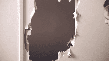 Woman peeking guiltily through a hole in the wall