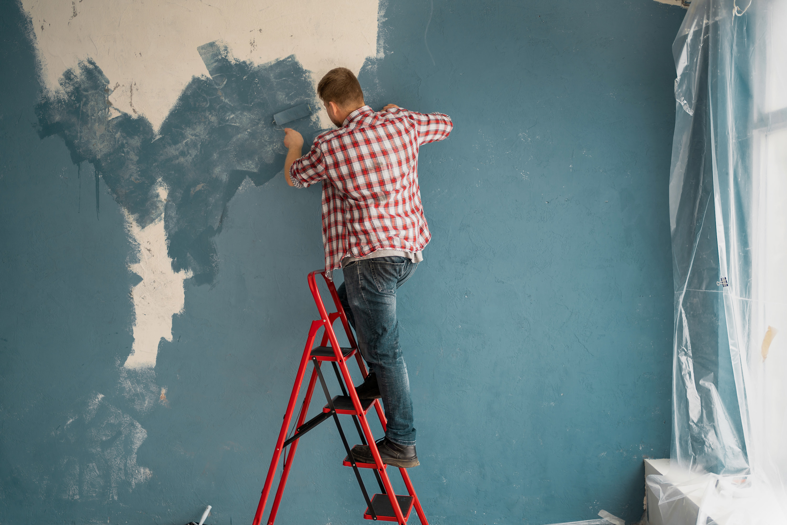 Man doing a bad job painting a room blue