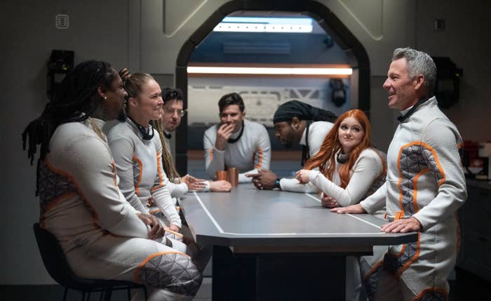 Contestants gather around a table in the Hub