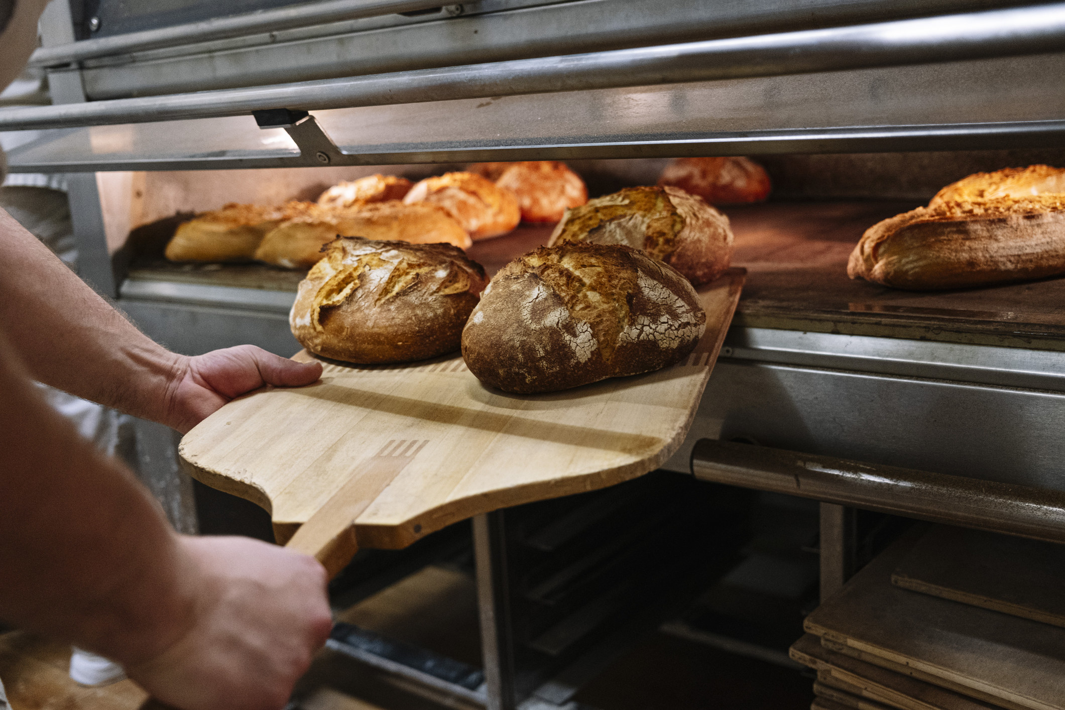 Chef removing baked bread from oven at bakery.