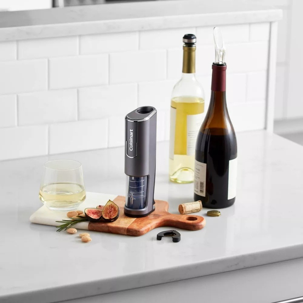the gray wine opener next to two bottles of wine and a glass