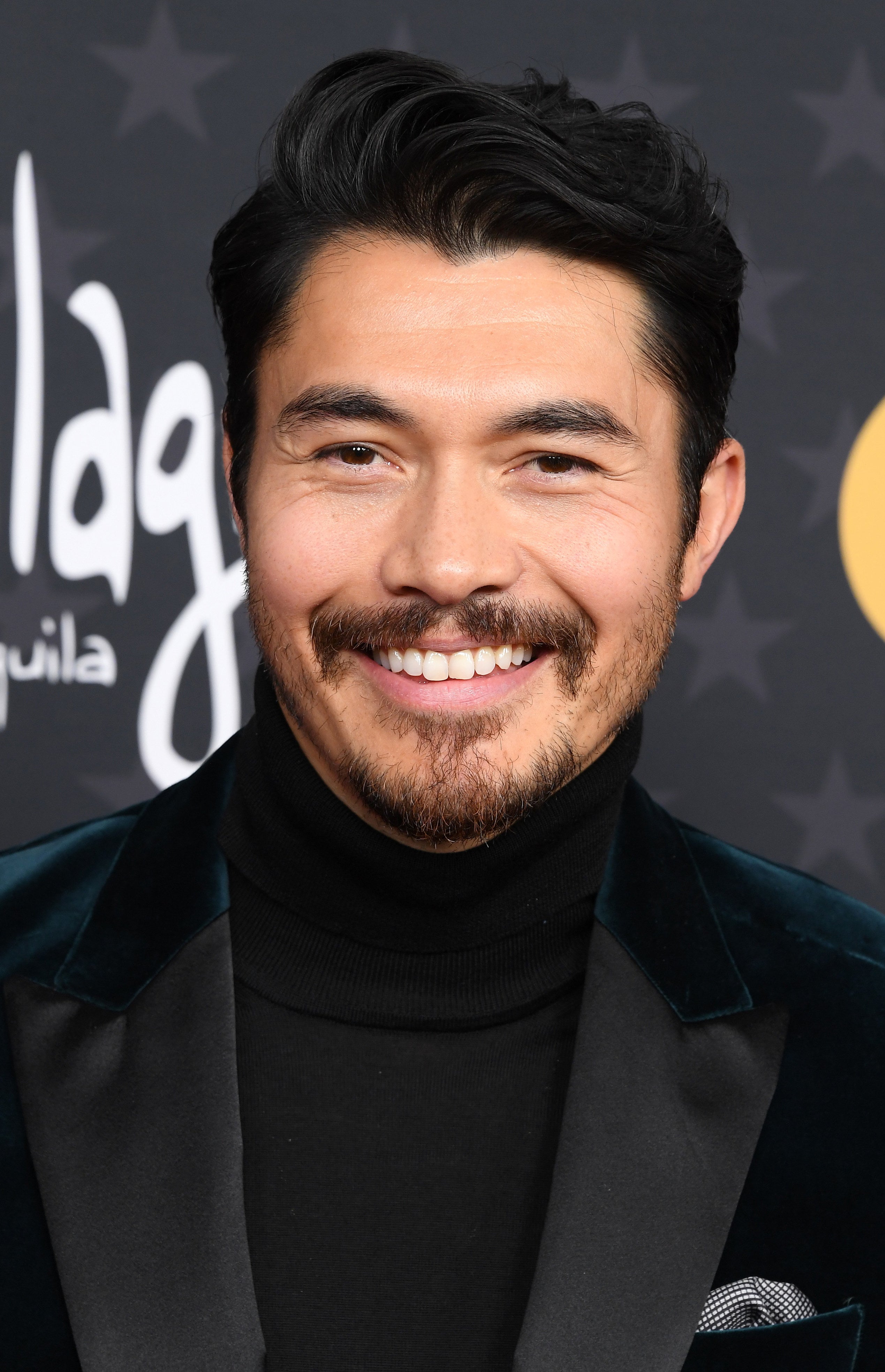Close-up of Henry Golding smiling in a turtleneck