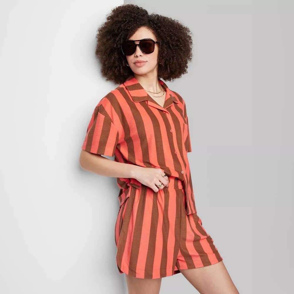 A model in the brown and coral striped shirt and shorts set
