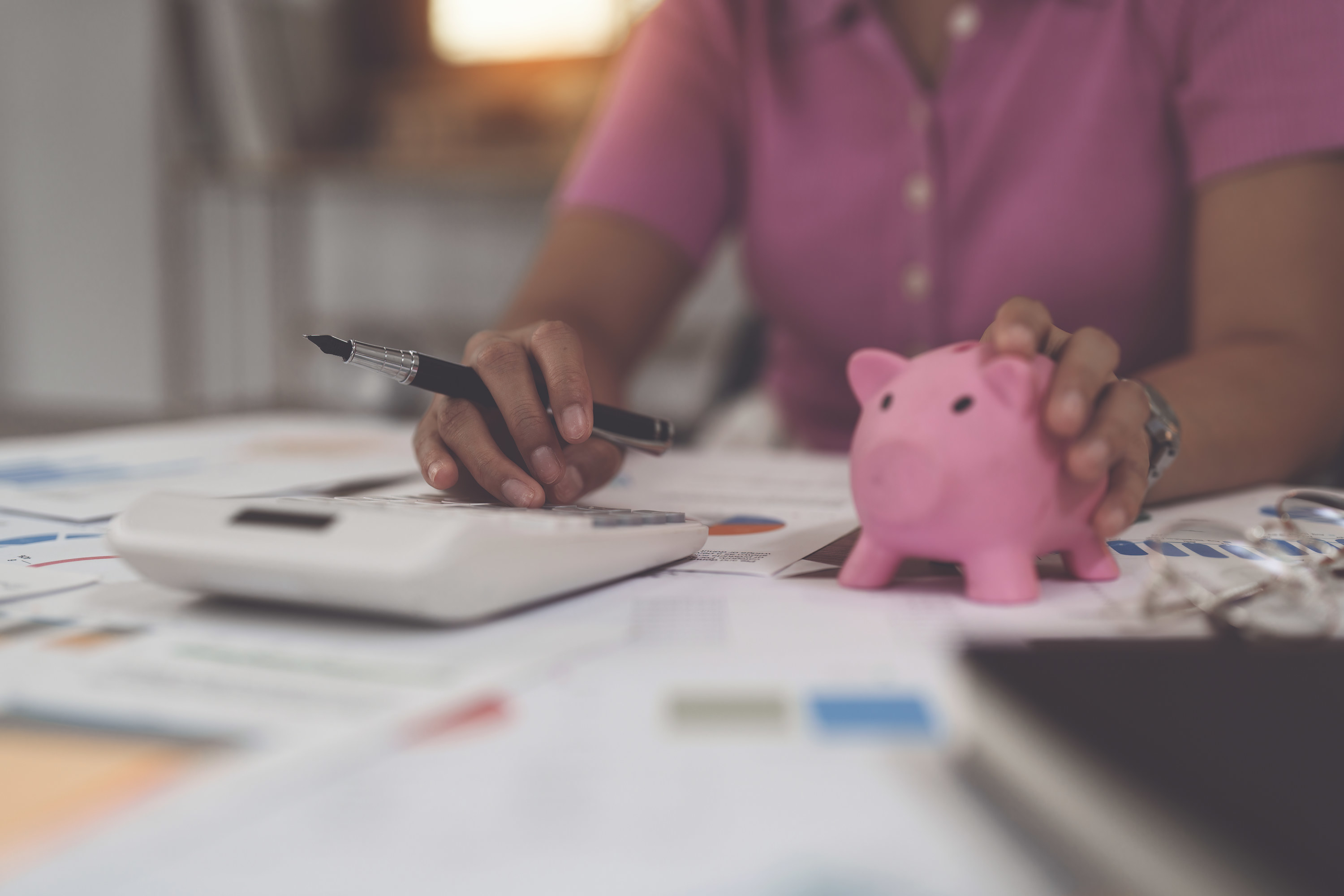 A woman calculates her financial savings with a piggy bank in hand