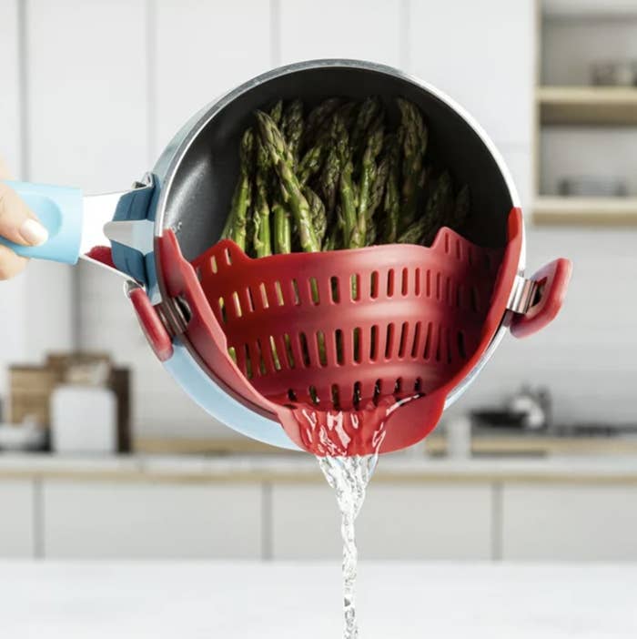 Someone pouring water out of a pot of asparagus with the red strainer clipped onto pot