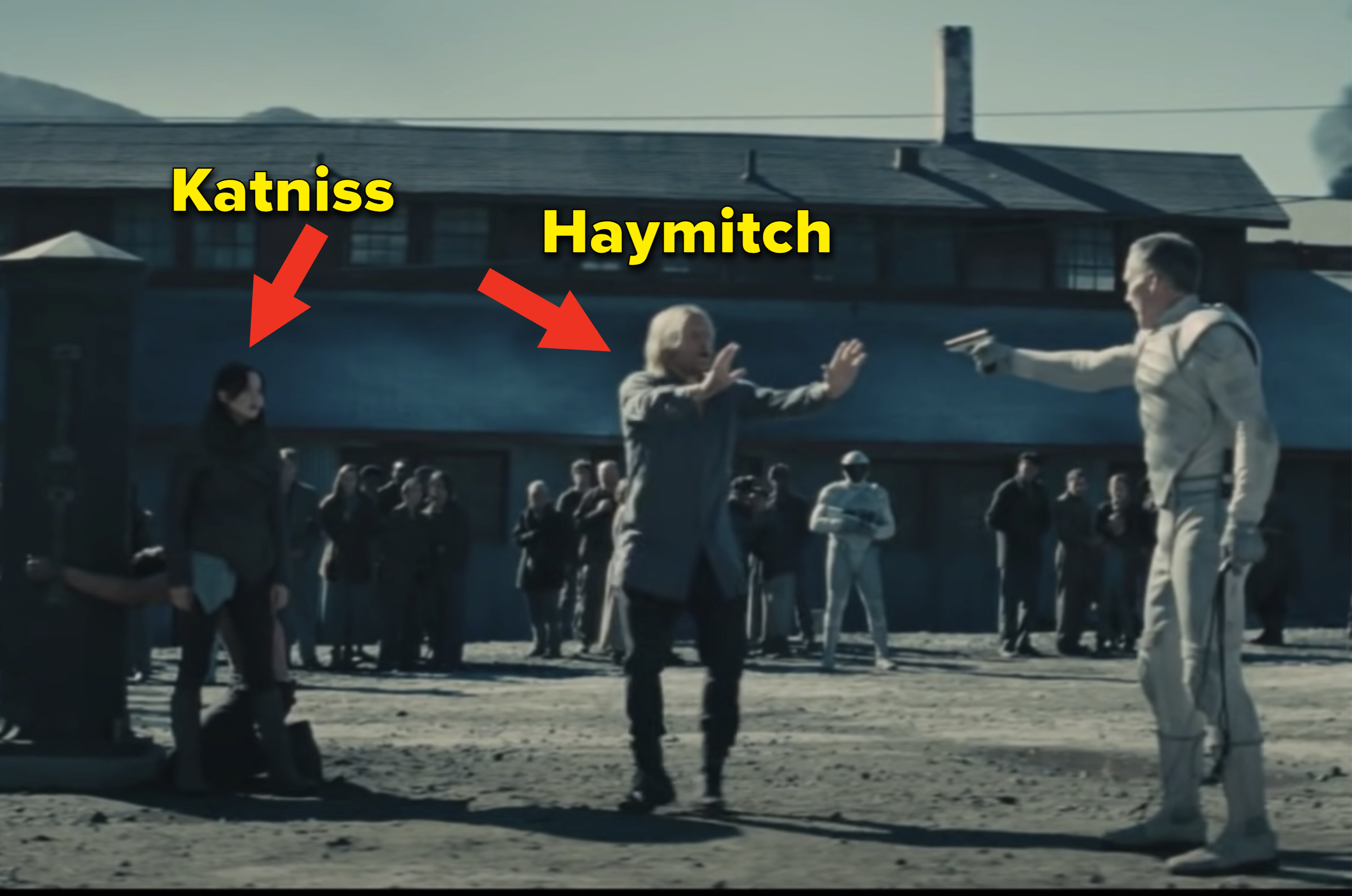 Haymitch standing between a guard with a gun and Katniss