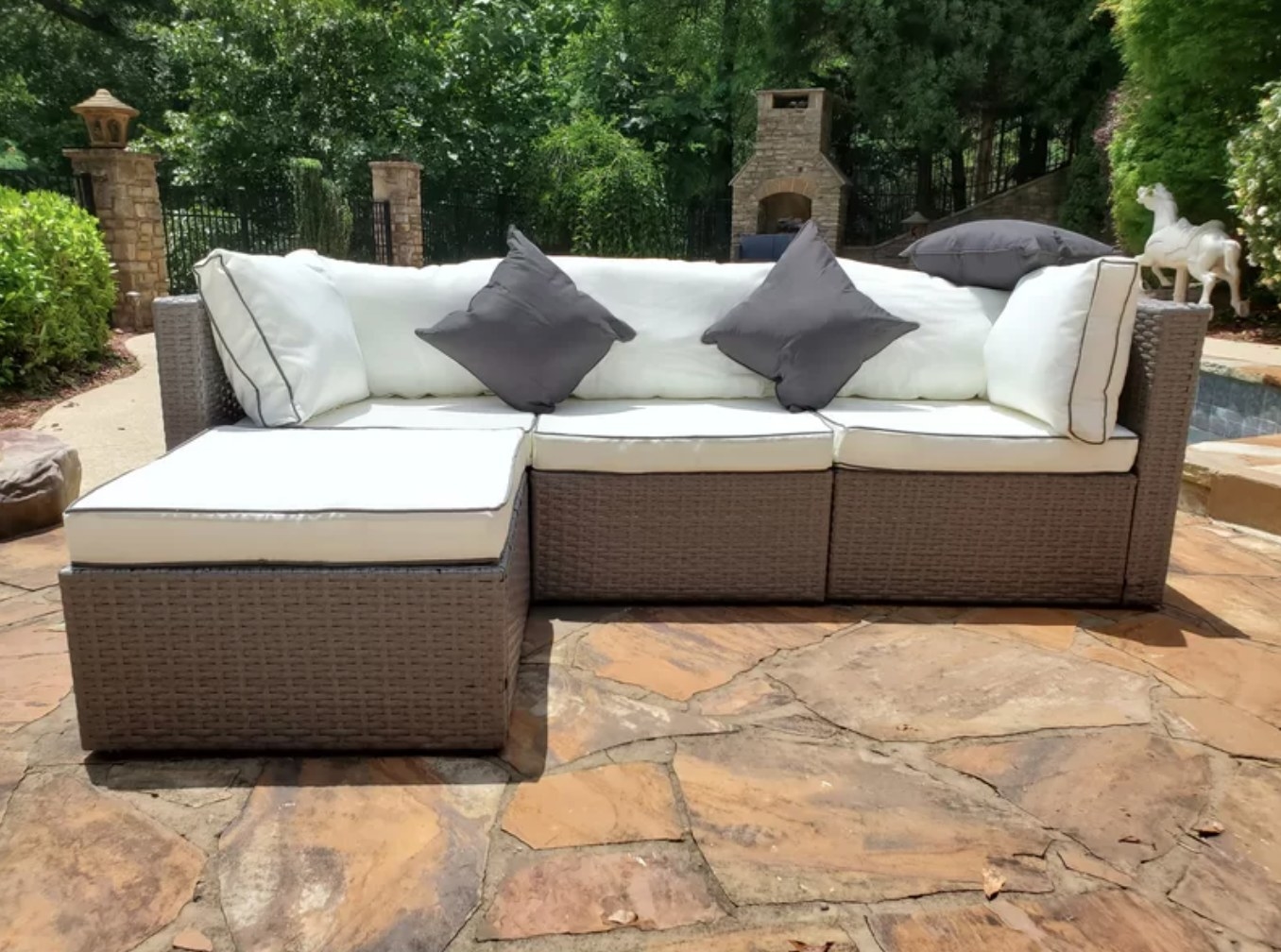 the dark wicker sofa with light cushions on a stone patio with trees in the background