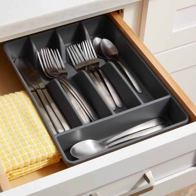 a gray silverware organizer in a shelf holding spoons, forks, and knives