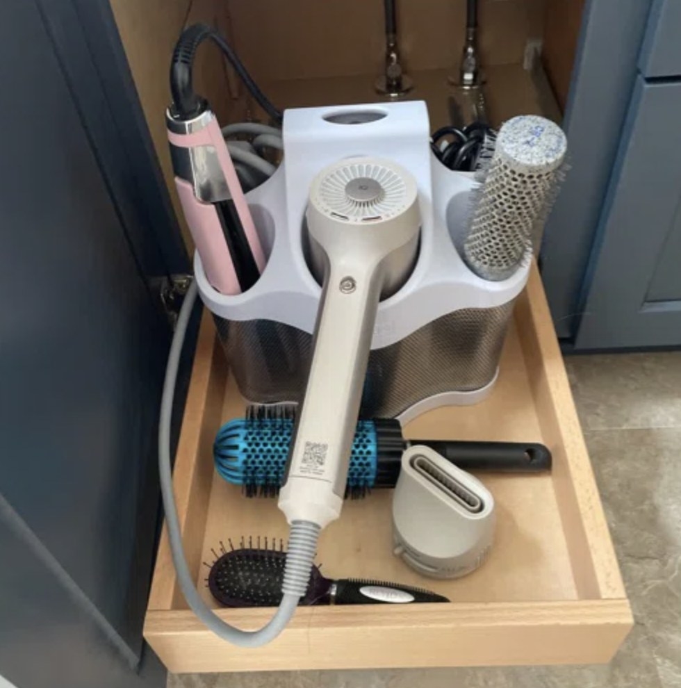 Reviewer's caddy on shelf underneath kitchen sink with hair dryer, straightener, and rolling brush with various other accessories