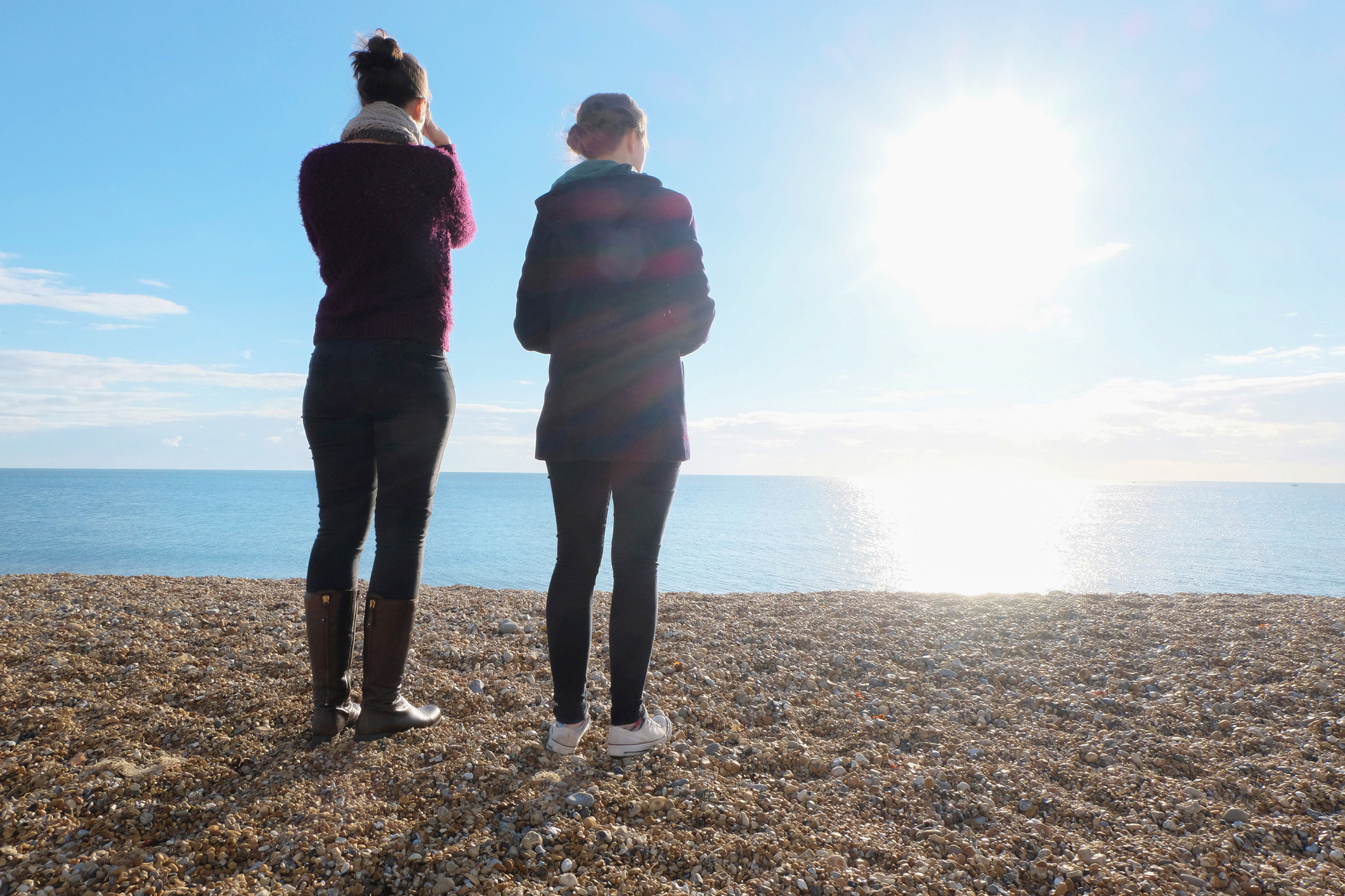 Two women standing on a beach looking out at the ocean