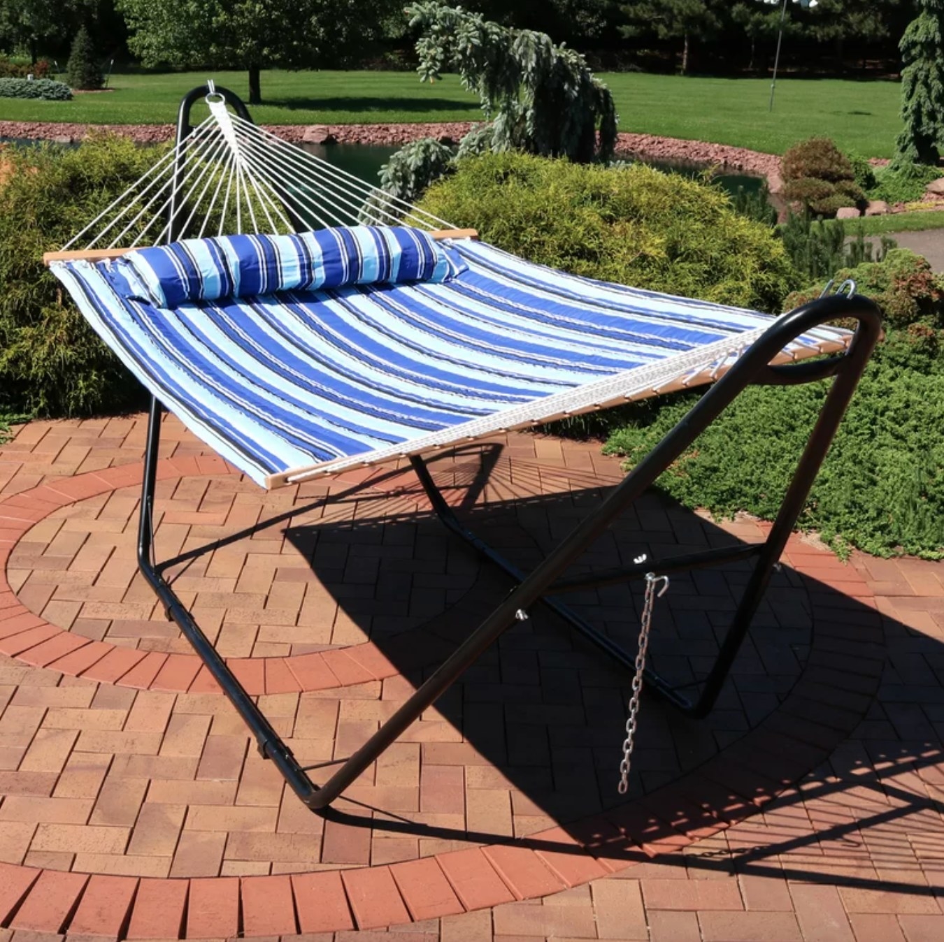 the blue striped hammock on a black metal frame on a brick patio in a garden