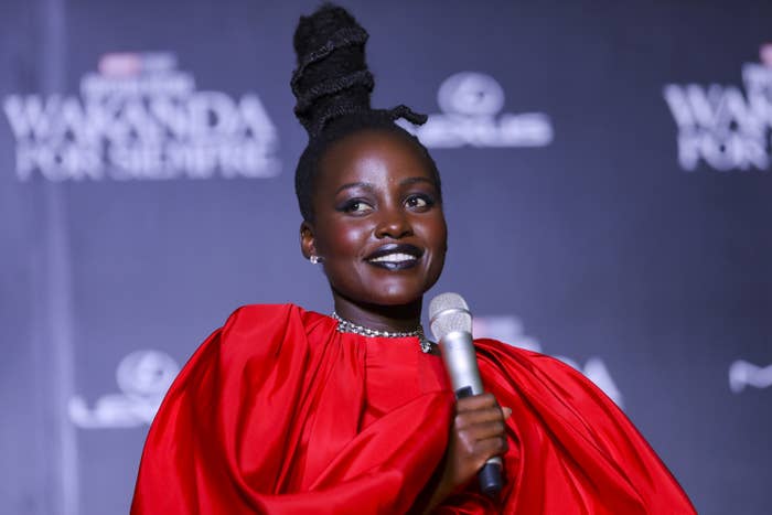 Lupita onstage holding a microphone and rocking a large topknot
