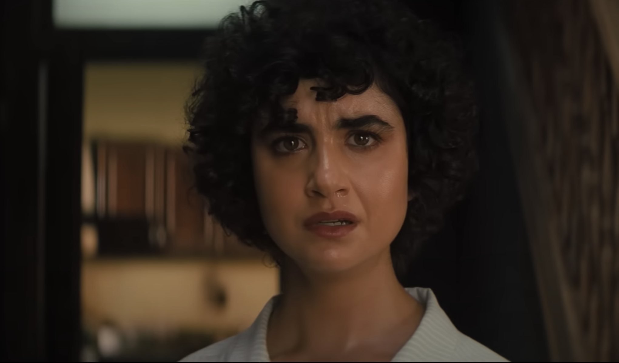 A young woman tears up as she looks, horrified, at something we can't see