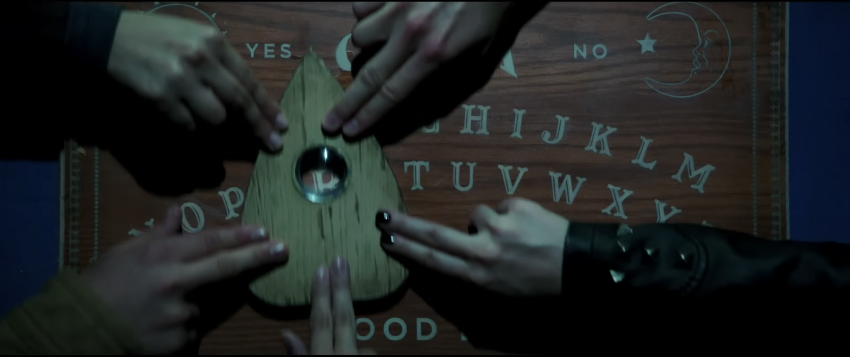 Five hands move a planchette around a Ouija board