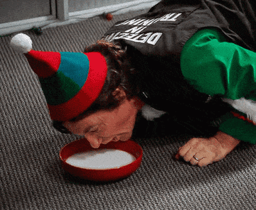 Jason Bateman licks milk out of a saucer on a carpeted floor