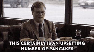 A bespectacled man in a suit comments on his assignment to eat 15 consecutive pancakes