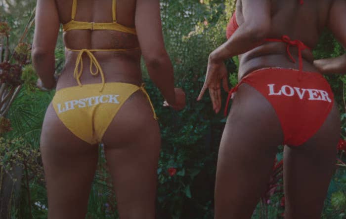 Two people in bikinis. The person&#x27;s on the left has a bikini bottom that says &quot;lipstick&quot; and the person on the right has a bikini bottom that says &quot;lover&quot;