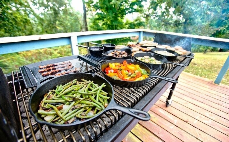 the black skillets with heated veggies and meat on a grill