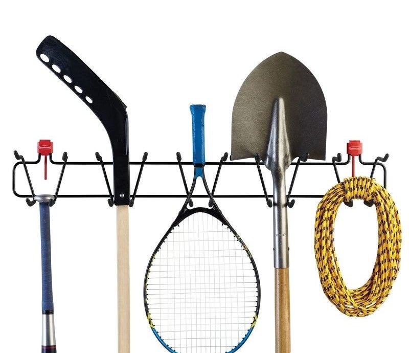 a sport and tools rack holding a tennis rack, shovel, rope, hockey stick, and bat