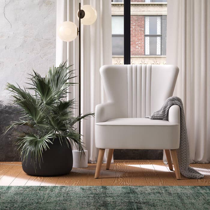 White accent chair with wooden legs, gray blanket draped over it