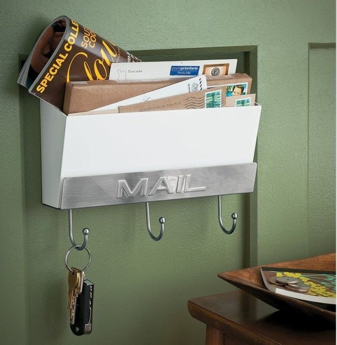 a mail holder attached to a green wall holding keys and letters by a small table