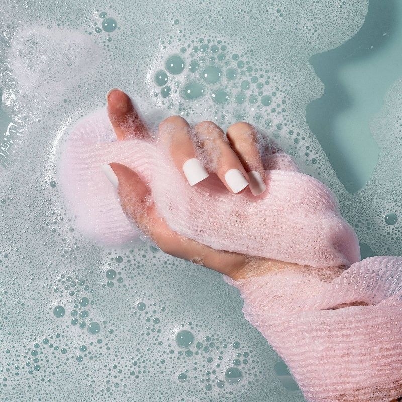 A person with a white manicure holding a pink bath towel in a tub of water