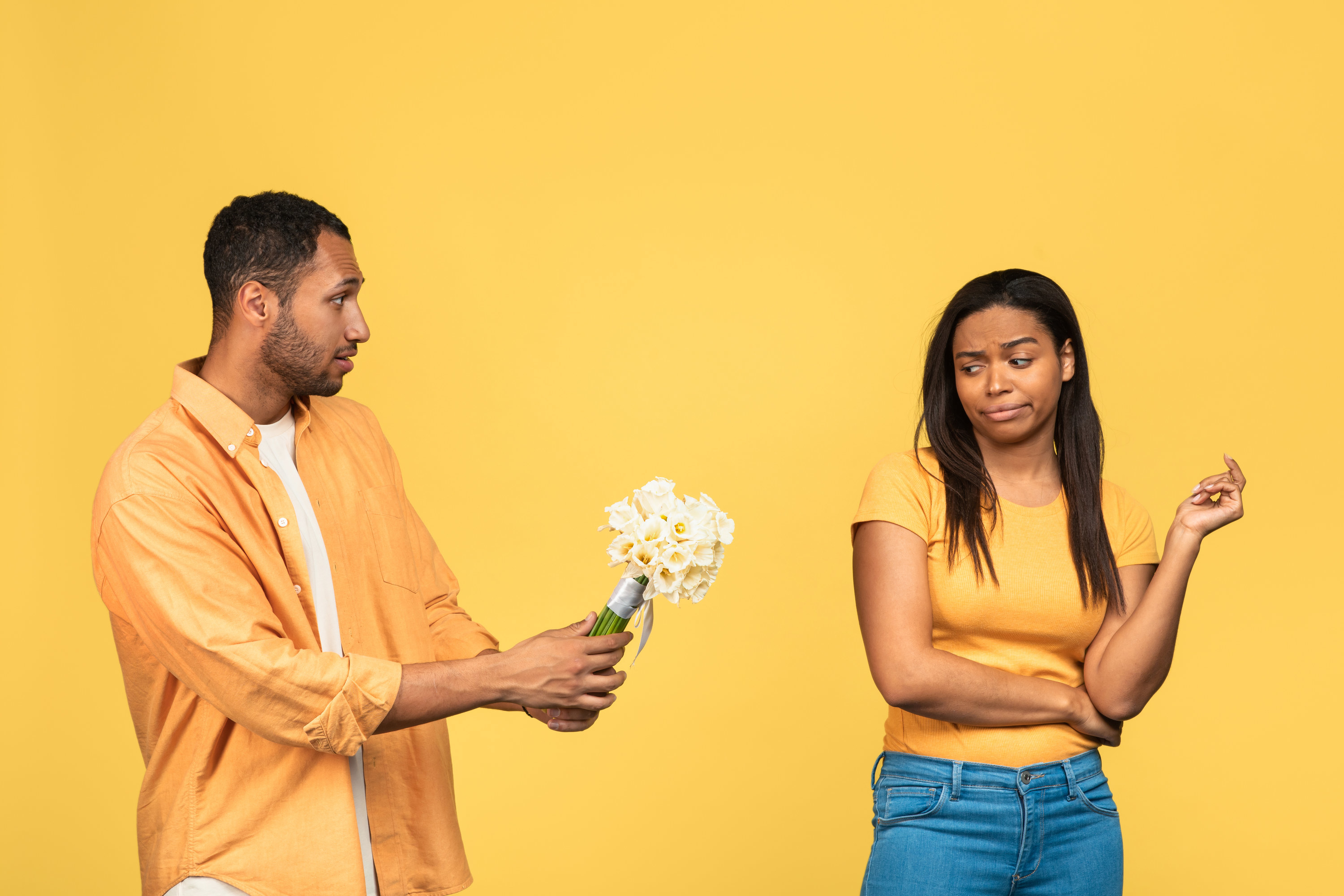 A man trying to give a woman flowers while she looks at them skeptically