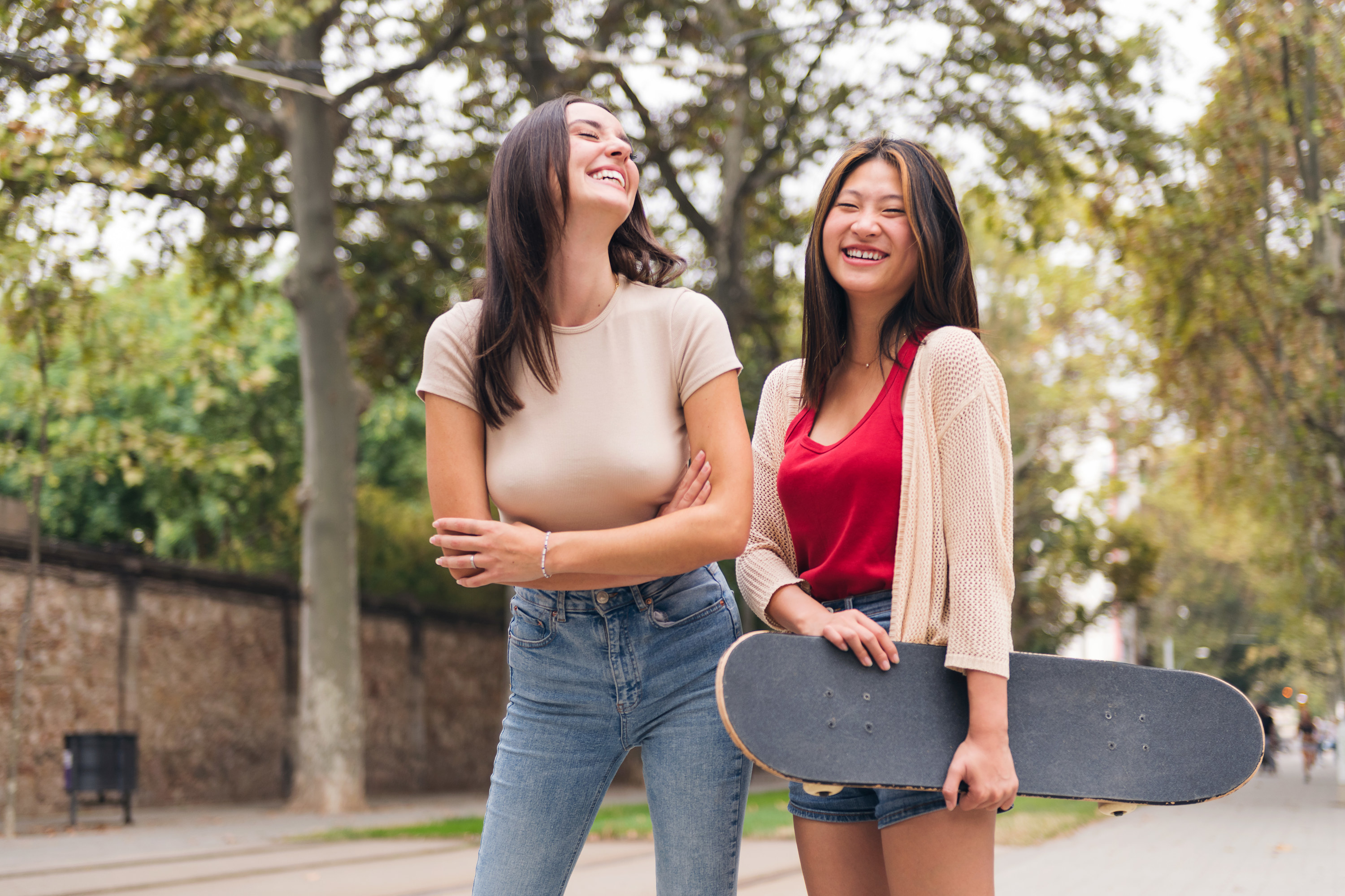Two women laughing while one holds a skateboard