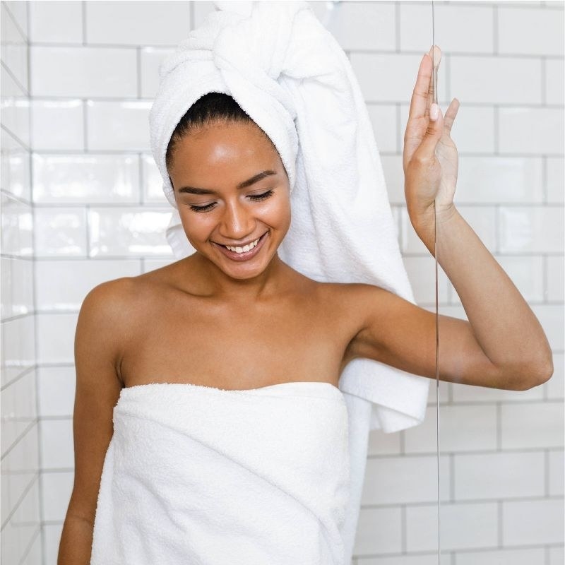 A person wearing a head and body towel getting out of the shower