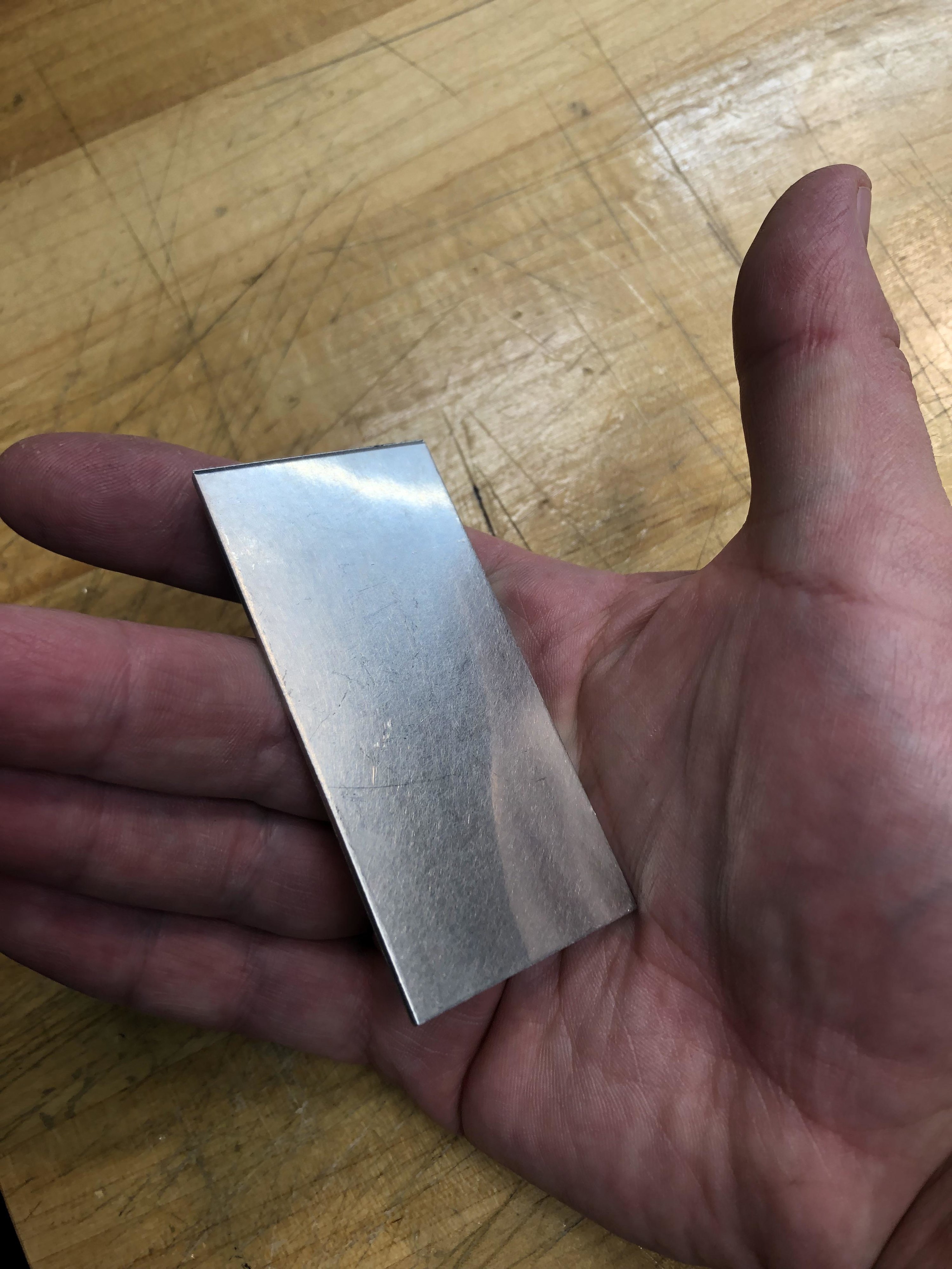 A hand holding a very thin, small rectangle of platinum