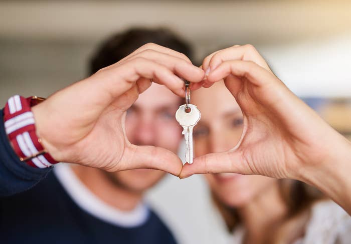 A couple form a heart shape with their hands while a key hangs in the center