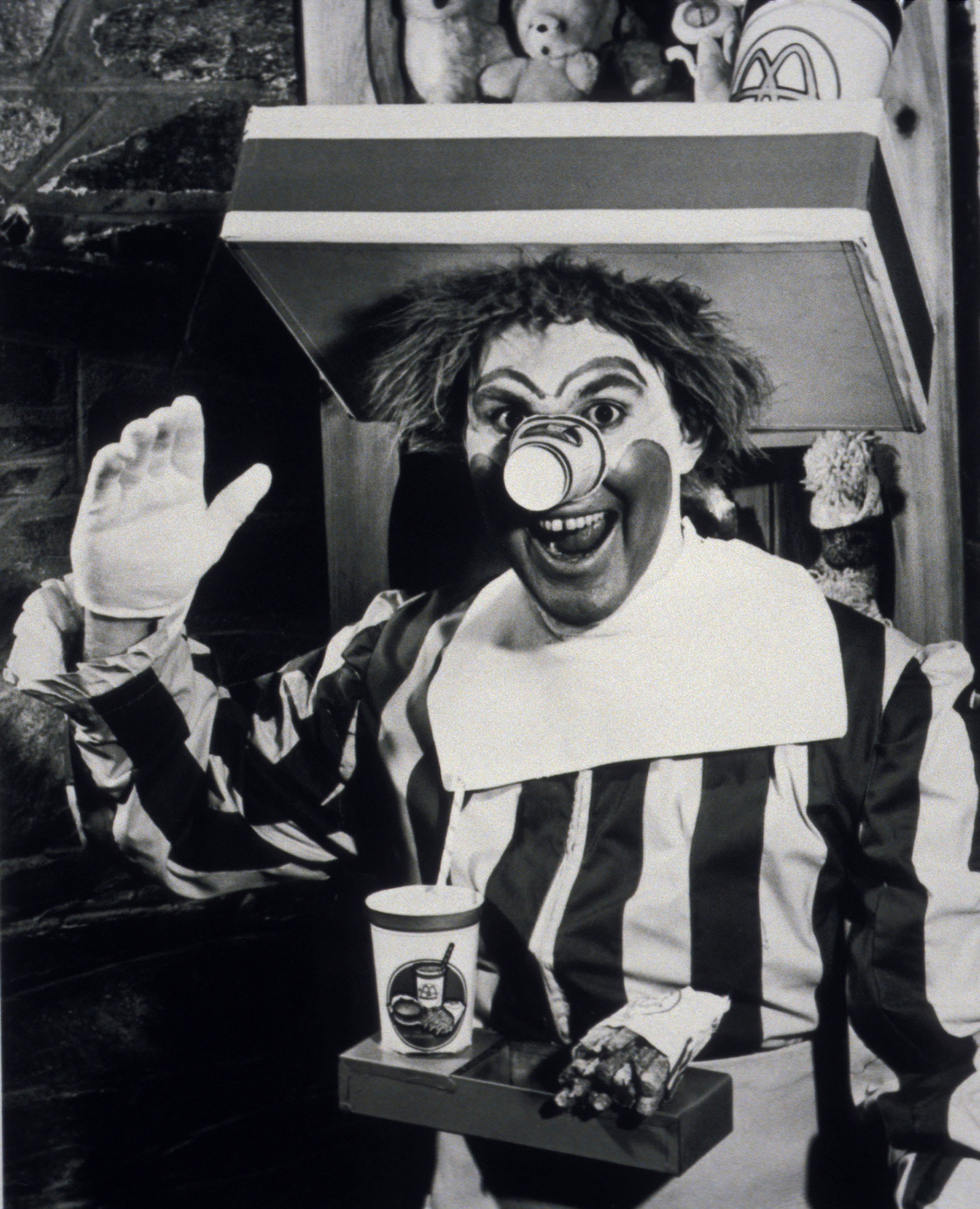 Man in a clown costume waving and smiling with a McDonald&#x27;s cup and fries in front of him