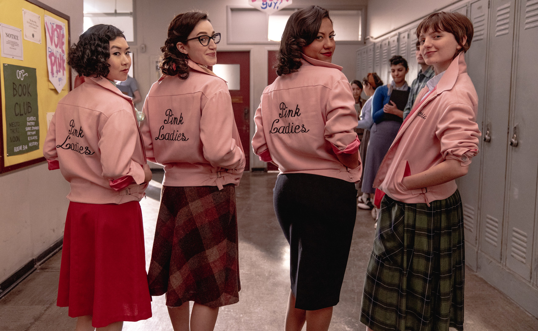 The Pink Ladies in a school hallway wearing their matching jackets and knee-length skirts