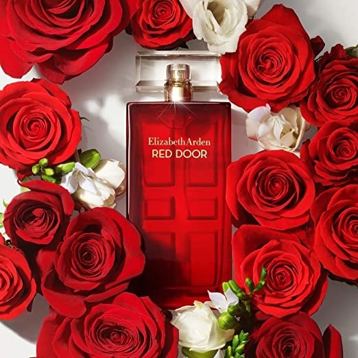 A photo of red perfume surrounded by red and white roses