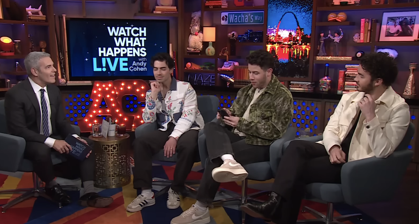 Nick looking through his phone as he sits with his brothers  on Watch What Happens Live!